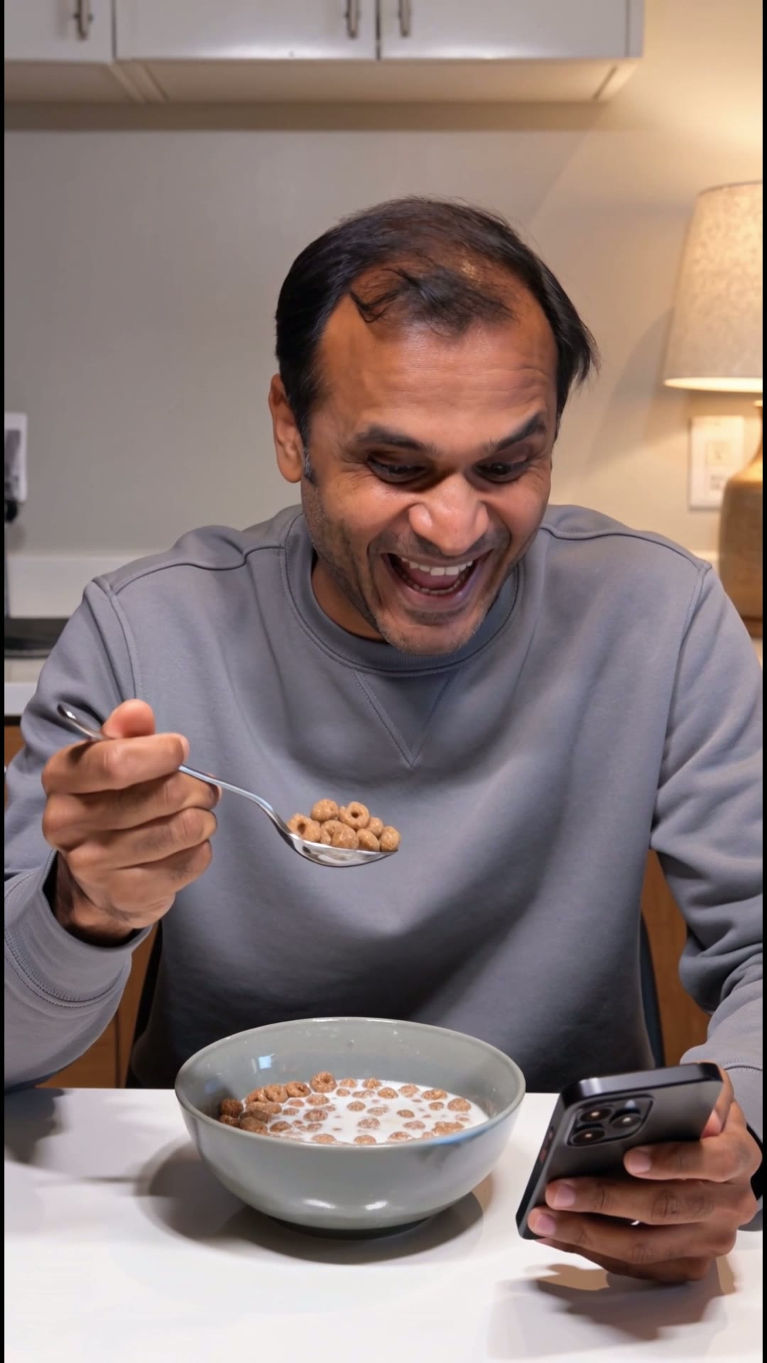 Amit Laughing at Phone Eating Cereal — Vertical
